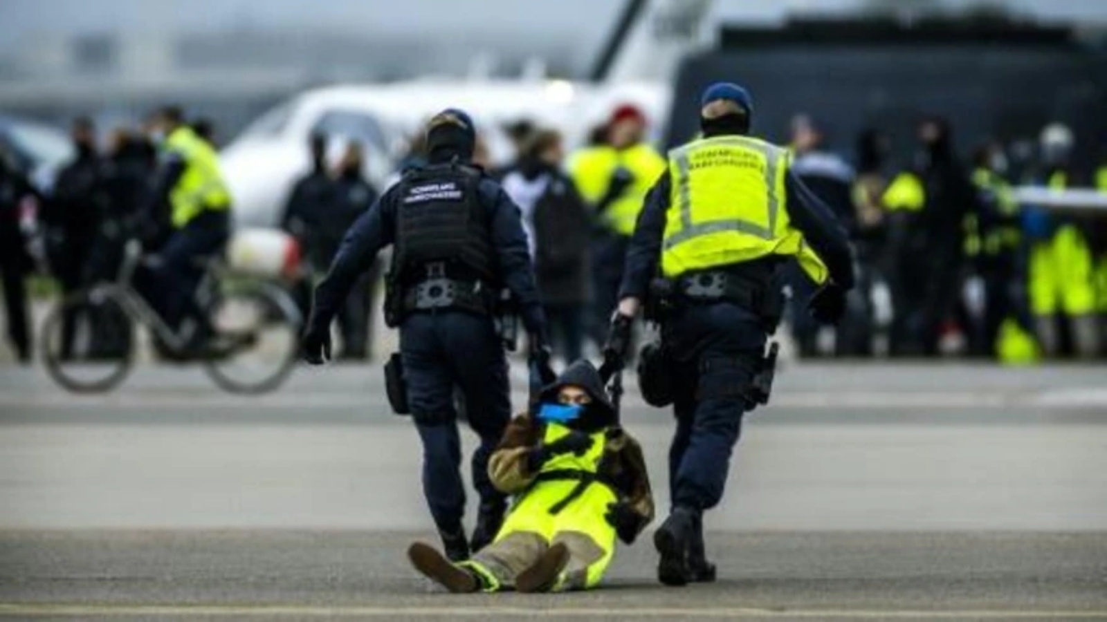 عنصران من الشرطة الهولندية أثناء توقيفها ناشطا بيئيا في مطار سخيبول في أمستردام بتاريخ 5 نوفمبر 2022