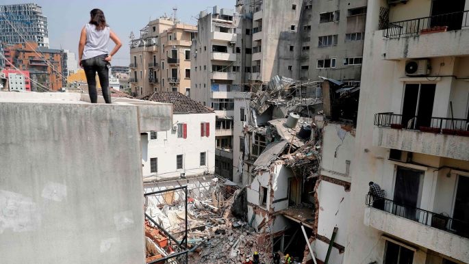 امرأة تنظر من فوق سطح أحد المنازل إلى أنقاض مبنى تضرر بشدة في العاصمة اللبنانية بيروت
