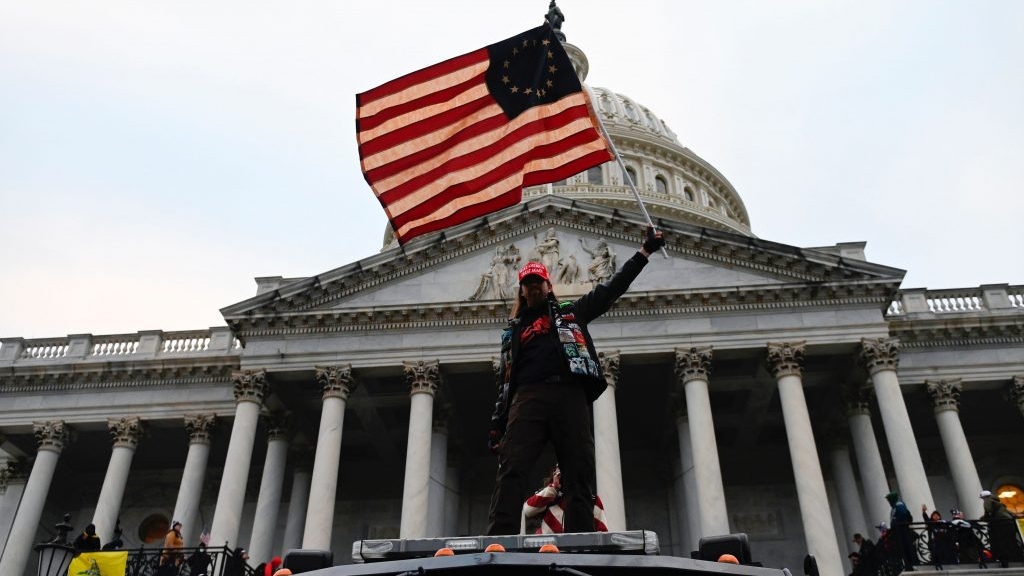 أحد مؤيدي ترمب يلوح بالعلم وهو يقف على سيارة حكومية أمام مبنى الكابيتول الأميركي في 6 يناير 2021