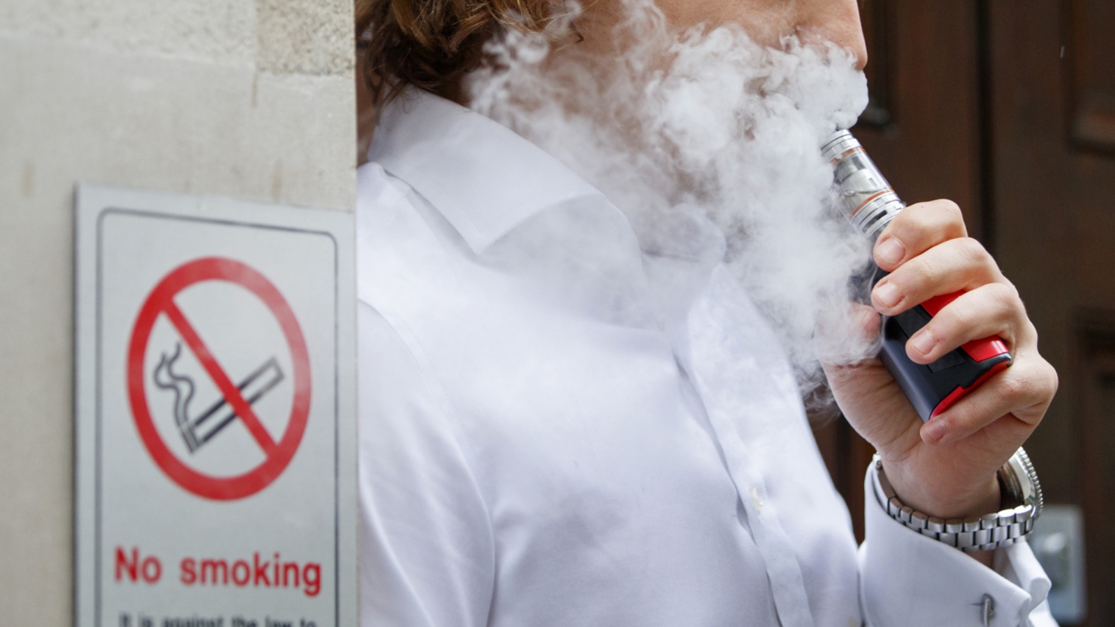 شاب يدخن سيجارة إلكترونية قرب لافتة 