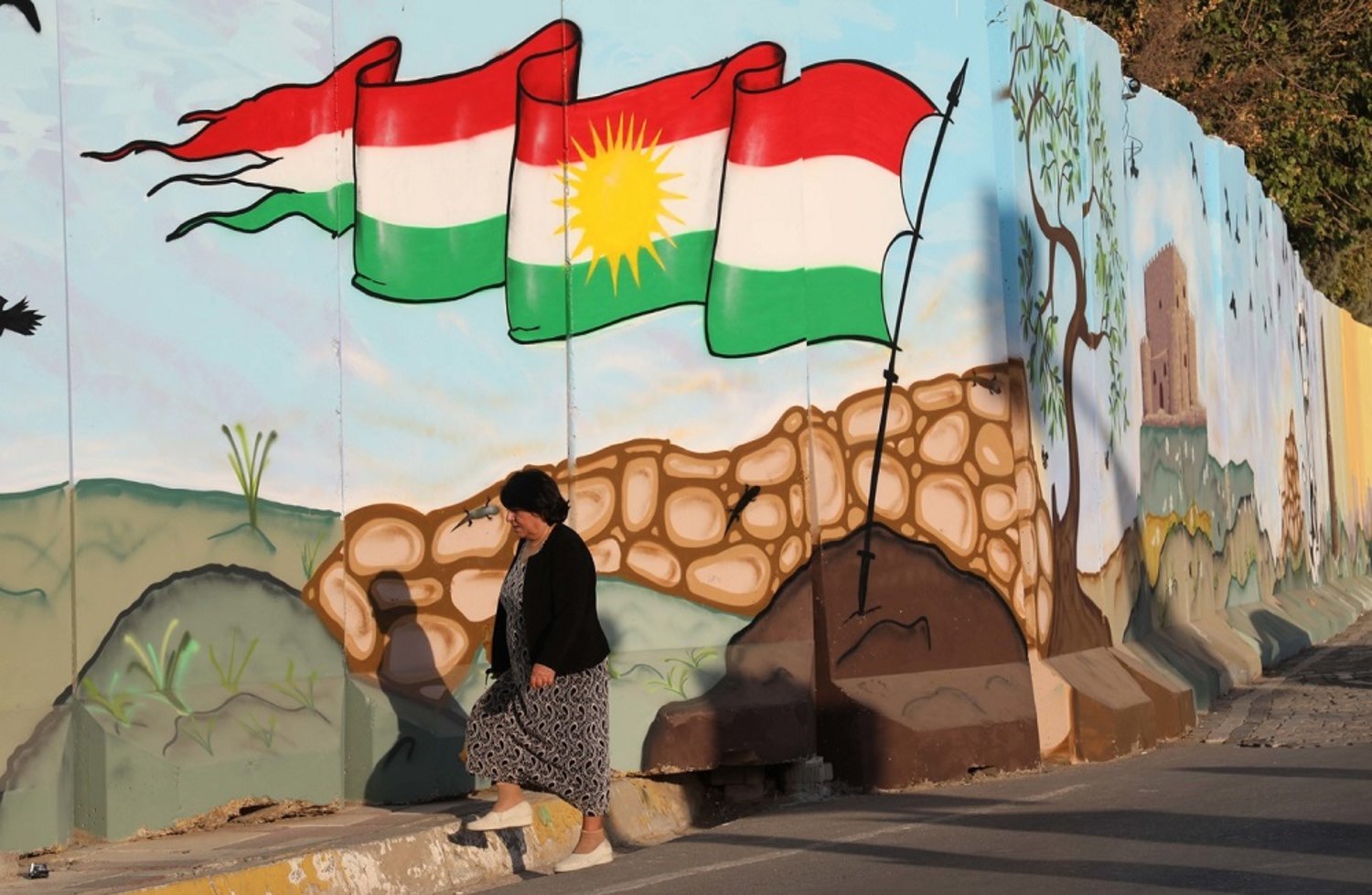 امرأة تسير بالقرب من جدار رسم عليه علم كوردستان