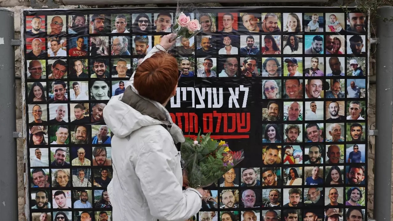 امرأة تحمل زهوراً أمام جدار عليه صور الرهائن لدى حماس في القدس، 12 شباط (فبراير) 2024