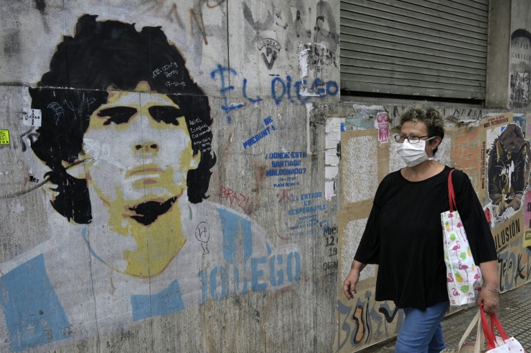 امرأة تسير قرب رسم على الجدران لنجم كرة القدم الأرجنتيني السابق دييغو مارادونا خلال الإغلاق التام الذي فرضته الحكومة في مواجهة انتشار فيروس كورونا المستجد، في بوينوس آيرس، في 22 نيسان/أبريل 2020.