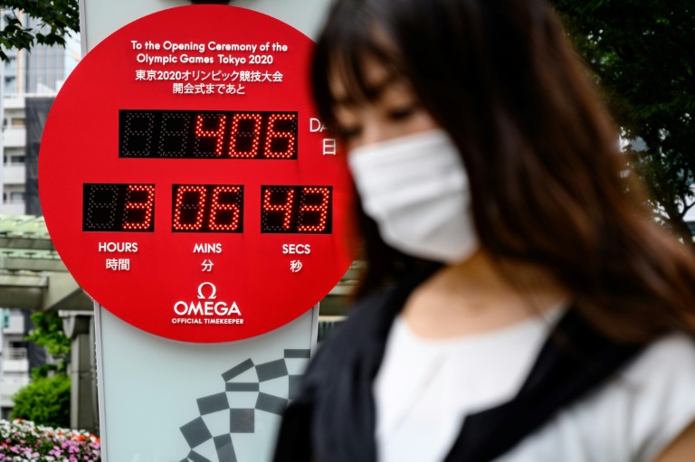 امرأة تضع كمامة واقية لدى مرورها الى جانب عداد لدورة الألعاب الأولمبية الصيفية في طوكيو في 12 حزيران/يونيو 2020.