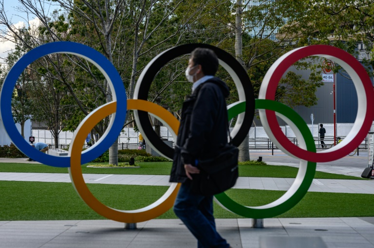 رجل يرتدي قناعا واقيا يمر بجانب الشعار الأولمبي في طوكيو، في 11 آذار/مارس 2020.