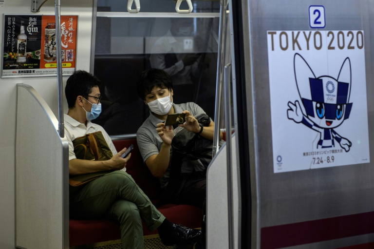 راكبان على متن قطار يرفع شعار دورة الألعاب الأولمبية في طوكيو، في صورة مؤرخة 13 تموز/يوليو 2020.