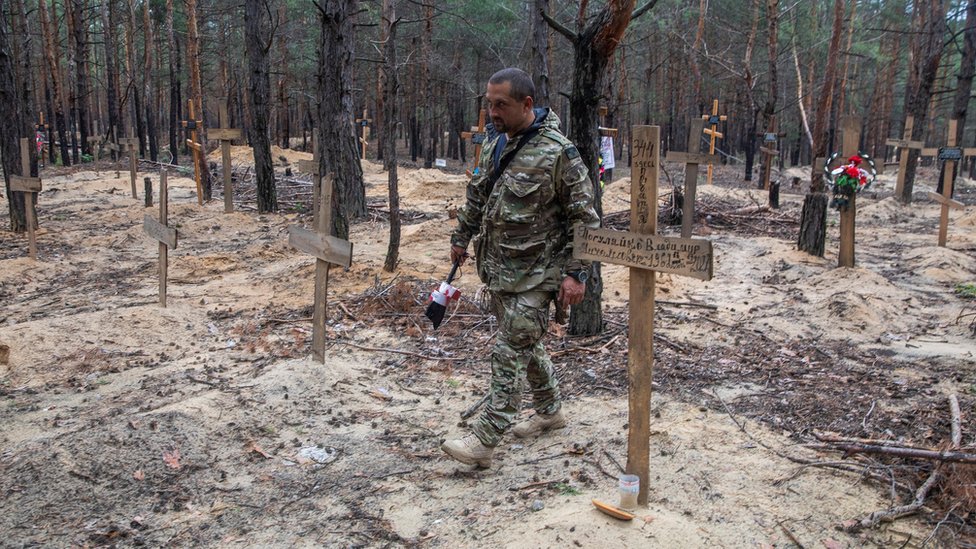 Reuters جندي أوكراني يمشي بين قبور يقول مسؤولون أوكرانيون إنه عثر عليها في غابة