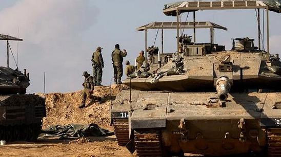 REUTERS | جنود إسرائيليون يتجمعون بالقرب من الدبابات بينما يتصاعد الدخان من غزة في الخلفية، بعد انتهاء وقف إطلاق النار