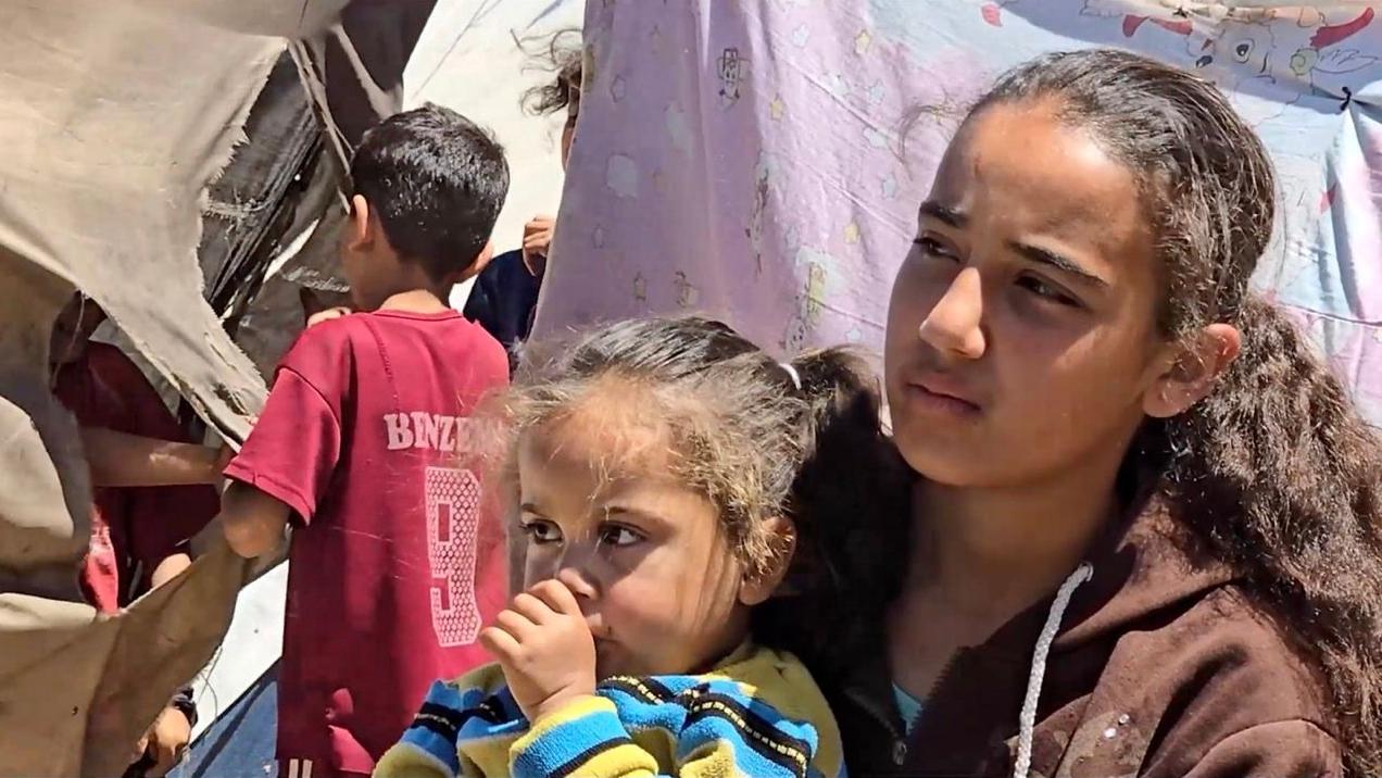 الطفلة الفلسطينية ليان تحمل شقيقتها الصفرى سوار
