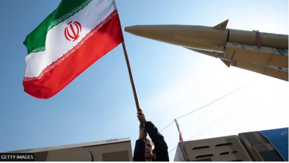 شخص يرفع علماً إيرانياً بجانب مجسم لصاروخ