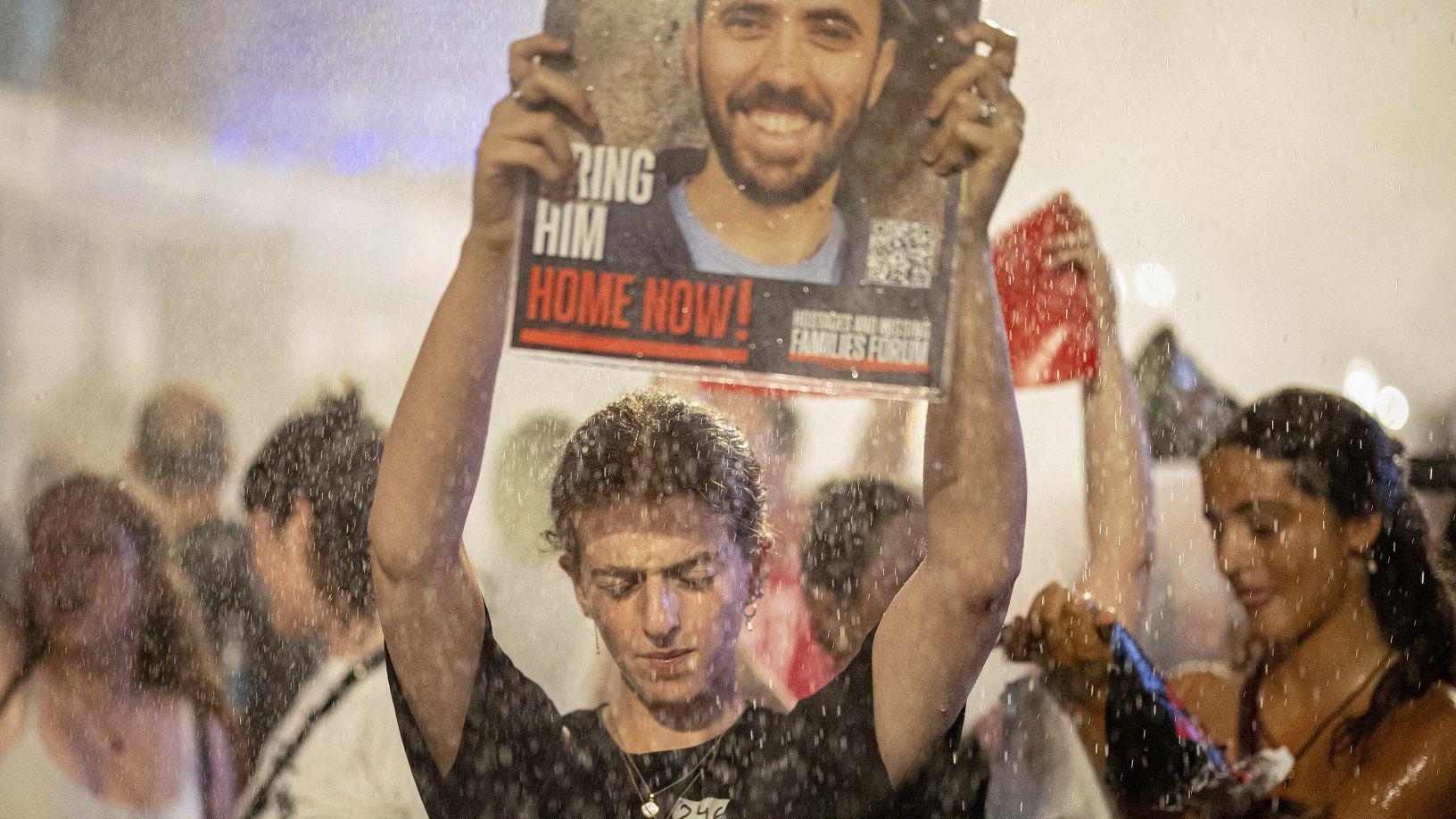 متظاهرون يحملون ملصقات بينما تنشر الشرطة الإسرائيلية خراطيم المياه، في مظاهرة ضد حكومة نتانياهو