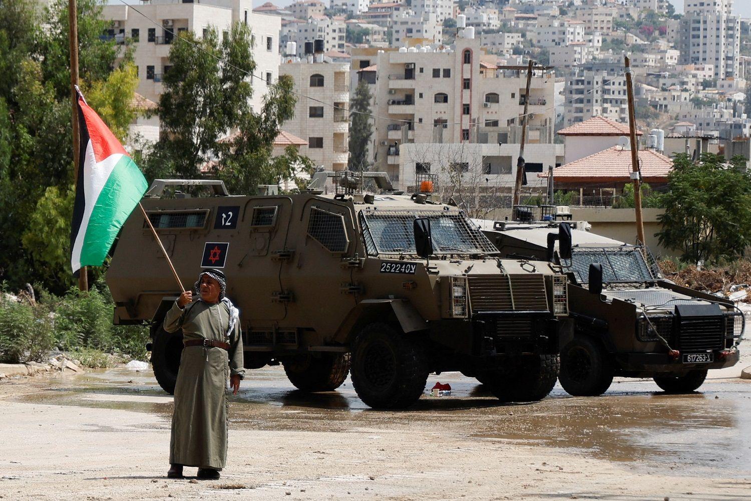 شخص يحمل العلم الفلسطيني أمام مدرعات الجيش الإسرائيلي في مدينة طولكرم في الضفة الغربية