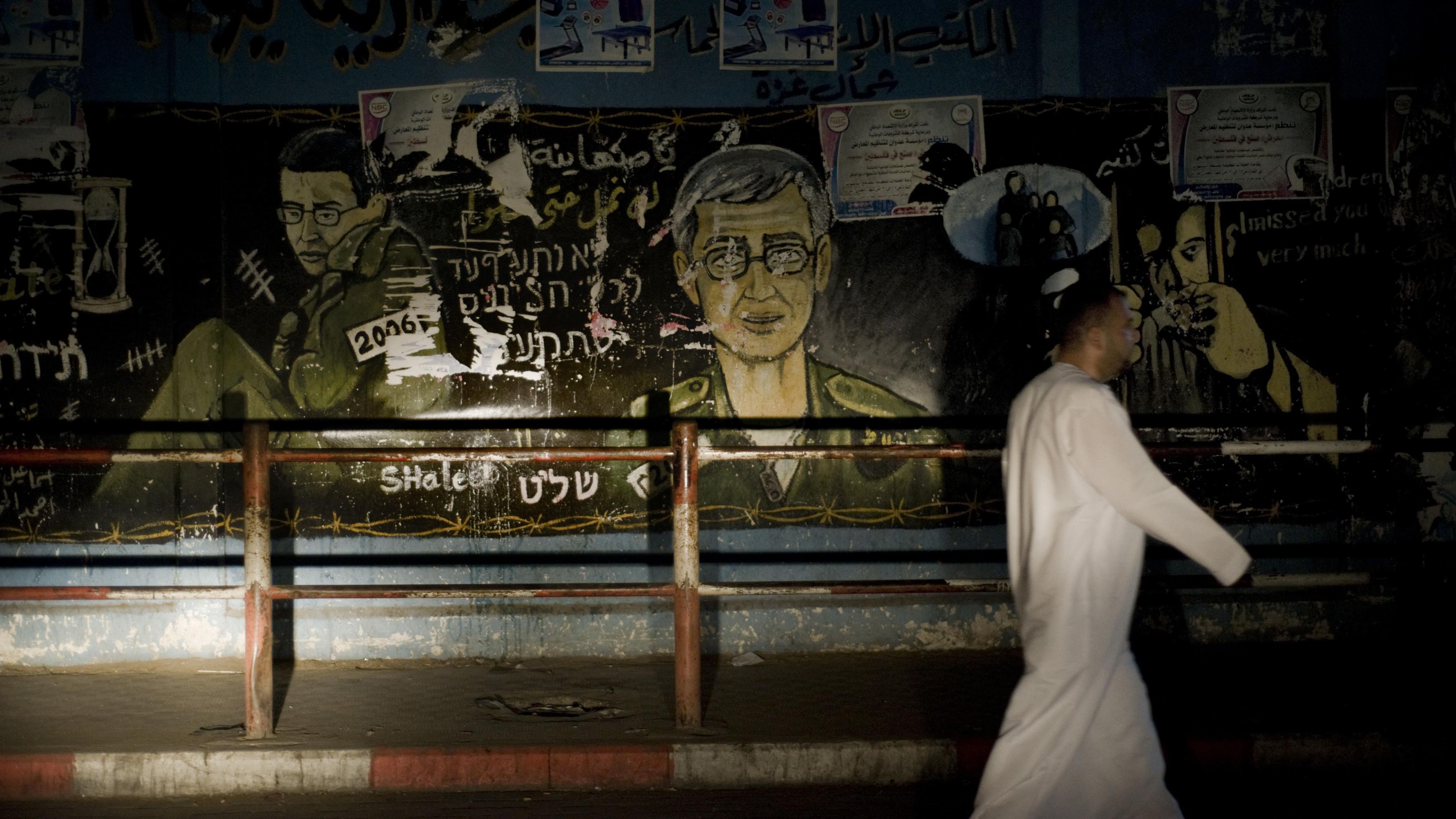 فلسطيني يمشي أمام لوحة جدارية تصور الجندي الإسرائيلي جلعاد شاليط شاباً وفي سن الشيخوخة في مخيم جباليا للاجئين، في شمال قطاع غزة، في 17 أكتوبر 2011