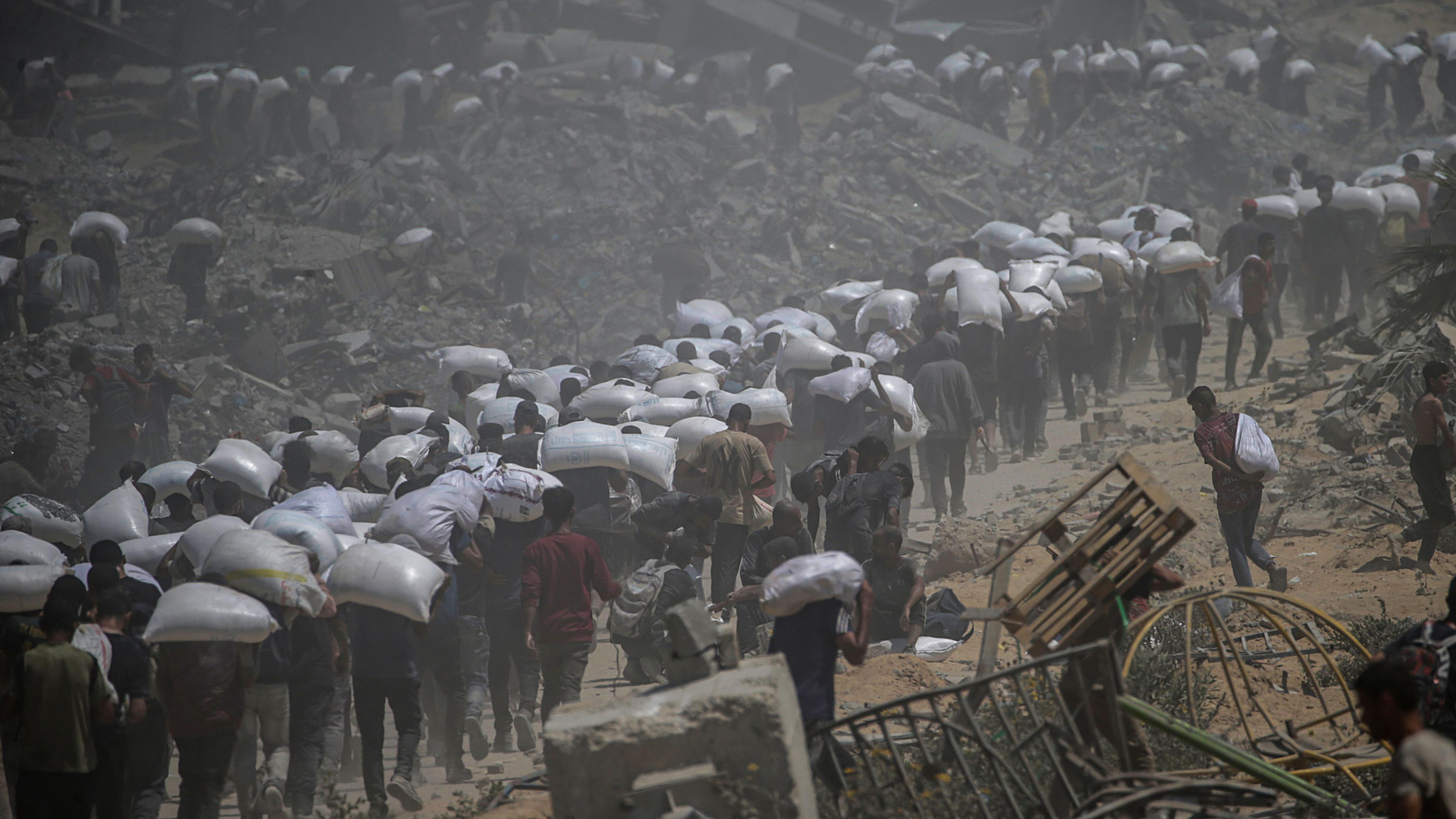 فلسطينيون يحملون أكياساً من الدقيق بالقرب من نقطة توزيع المواد الغذائية في معبر زيكيم في 27 يوليو/تموز 2025 - EPA