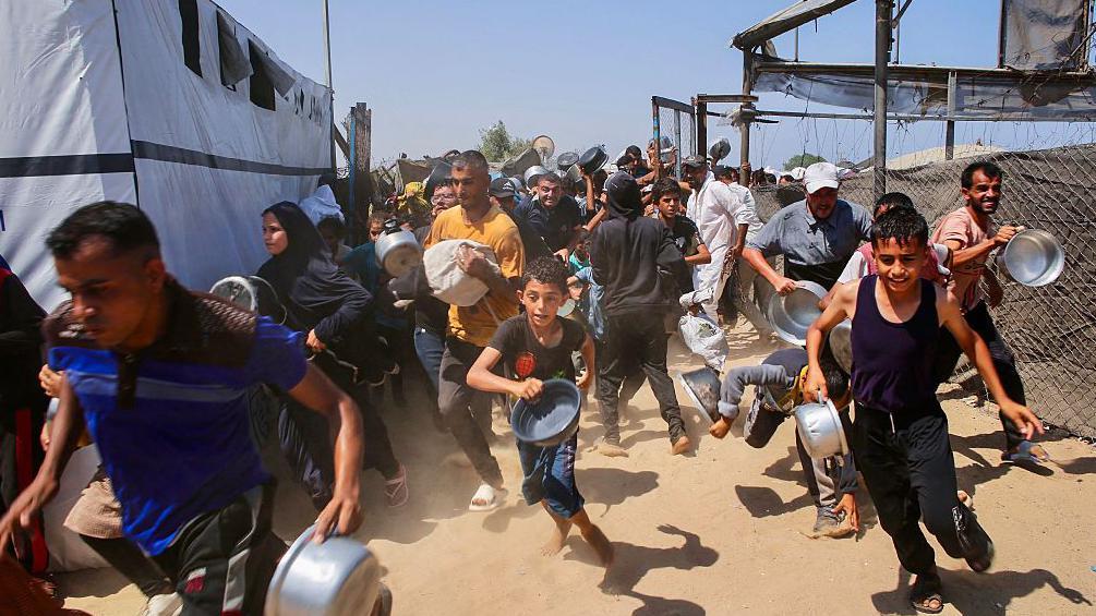 فلسطينيون يصطفون أمام مطبخ خيري لتلقي مساعدات غذائية - AFP