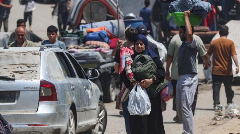 فلسطينيون يحملون أمتعتهم ويسيرون يجانب سيارات مدمرة في قطاع غزة - Reuters