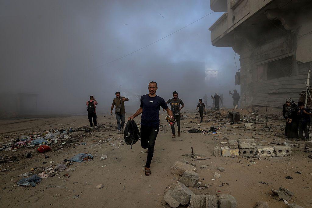 مجموعة من الأشخاص يحاولون النجاة من القصف الإسرائيلي، يركضون وسط أبنية مدمرة وداخن كثيف ناجم عن القصف الإسرائيلي على مدينة غزة. - Anadolu via Getty Images