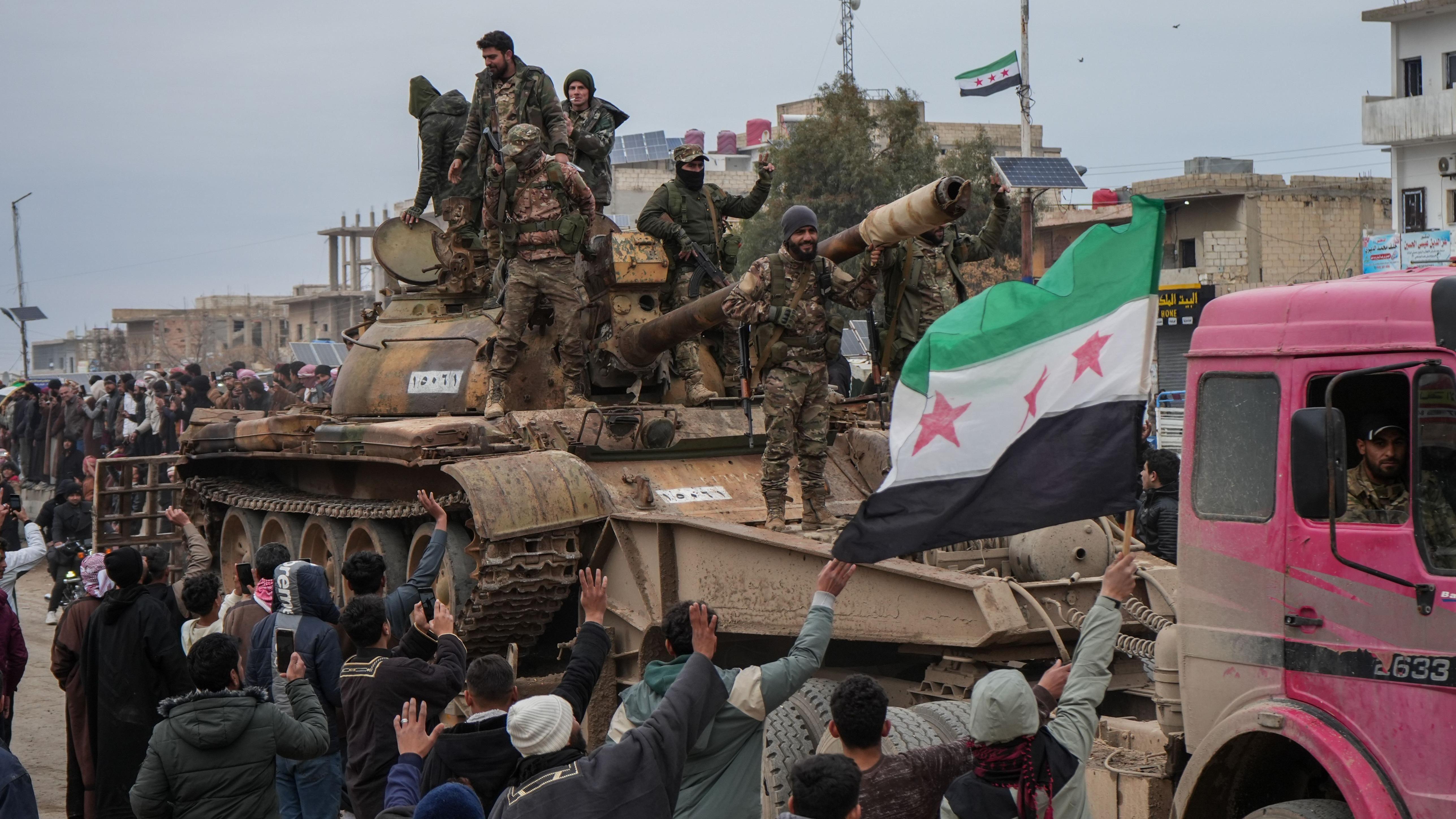 عناصر من الجيش السوري في دير حافر بعد انسحاب قوات سوريا الديمقراطية (قسد)، يقفون على ظهر دبابة ويحملون العلم السوري ذو النجوم الحمراء الثلاثة وحولهم حشد من الناس. - EPA