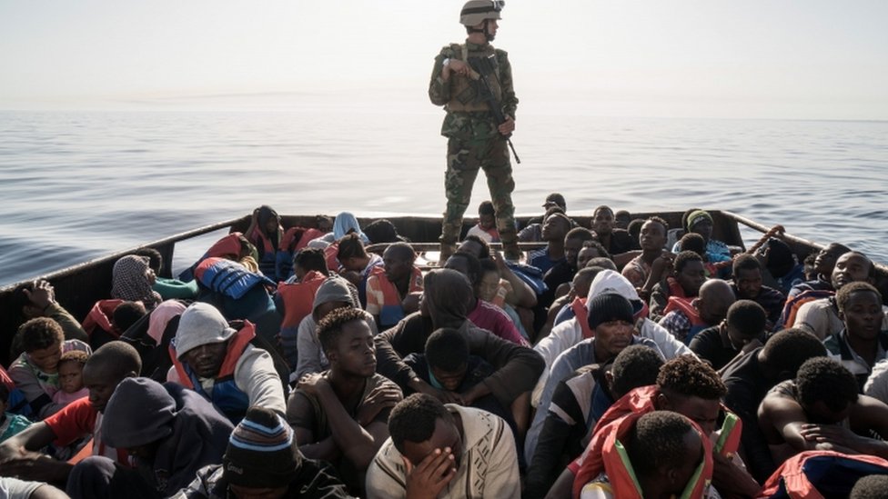 جندي ليبي يجرس قاربا مكتظا باللاجئين والمهاجرين