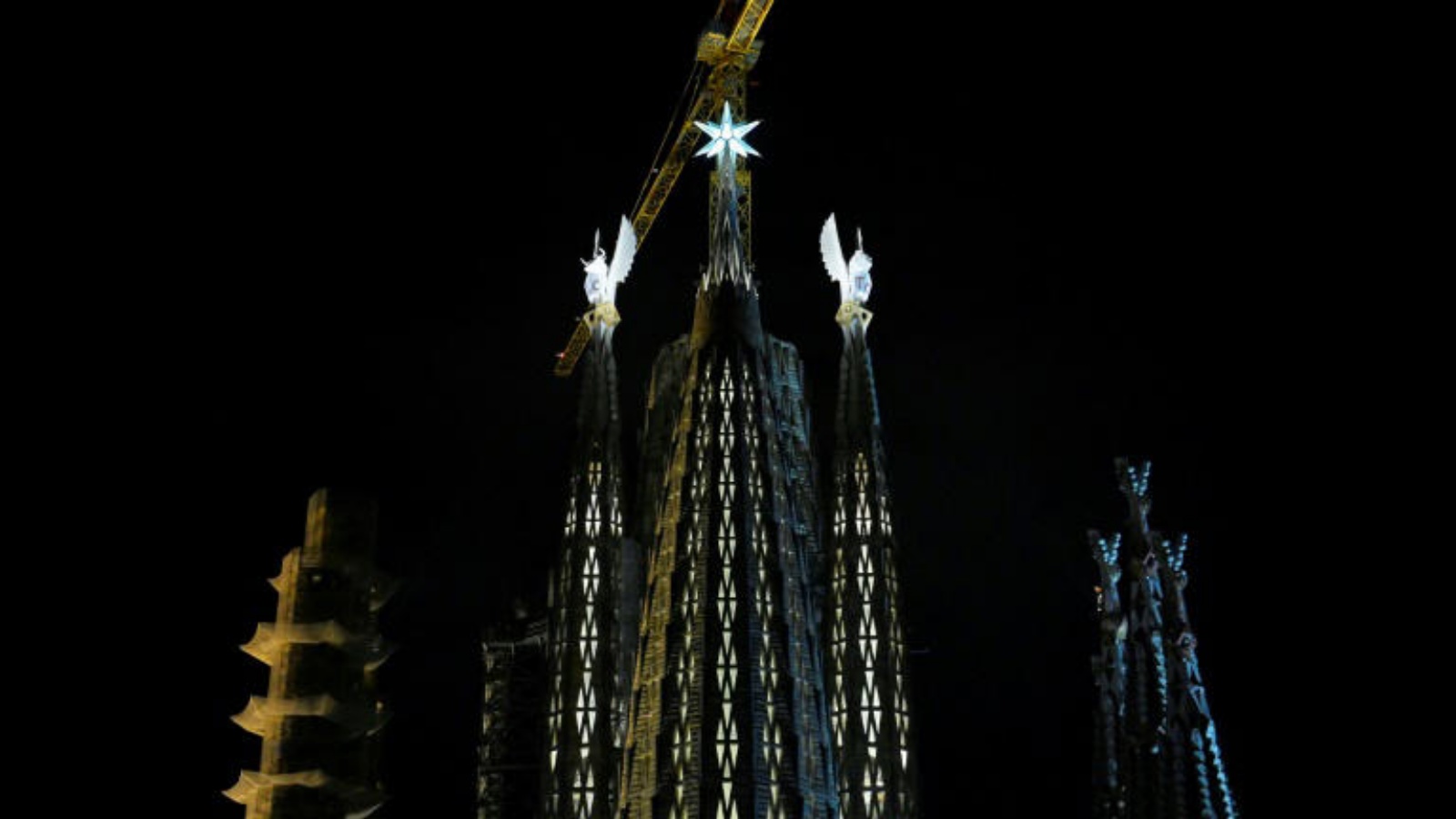 صورة التقطت في 16 ديسمبر 2022 لثلاثة من أبراج كاتدرائية ساغرادا فاميليا في برشلونة (إسبانيا) مضاءة وهي برج القديس لوقا (إلى اليسار) وبرج القديس مرقس (إلى اليمين) وبينها في الوسط برج العذراء مريم