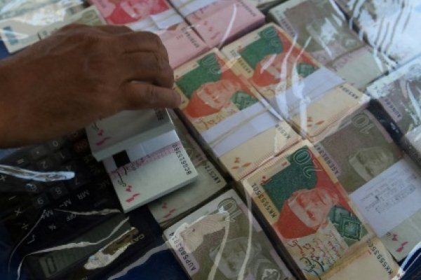 صراف عملة يرتب ورقات نقدية باكستانية في انتظار زبائن في شارع بكراتشي