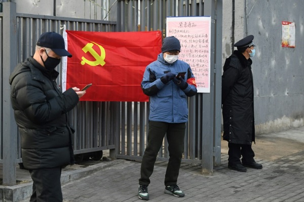 أناس يرتدون الأقنعة للاحتماء من فيروس كورونا المستجد قرب علم الحزب الشيوعي في بكين، 9 فبراير 2020