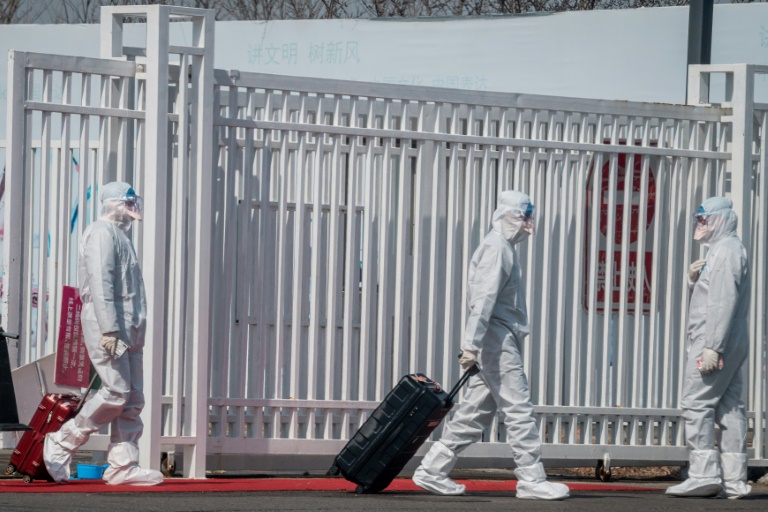 عمال يرتدون الملابس الواقية من فيروس كورونا ينقلون أمتعة الركاب في مطار الصين الدولي الجديد في 16 مارس 2020