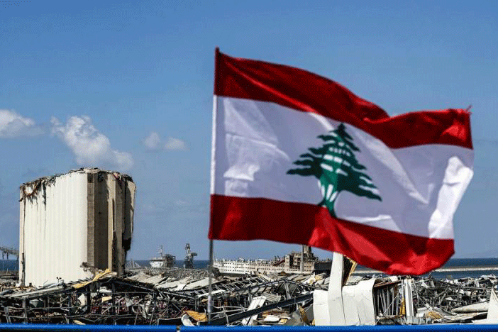 علم لبنان مرفوعاً بالقرب من مرفأ بيروت، وفي الخلفية اهراءات القمح التي أجهز عليها انفجار الثلاثاء الماضي