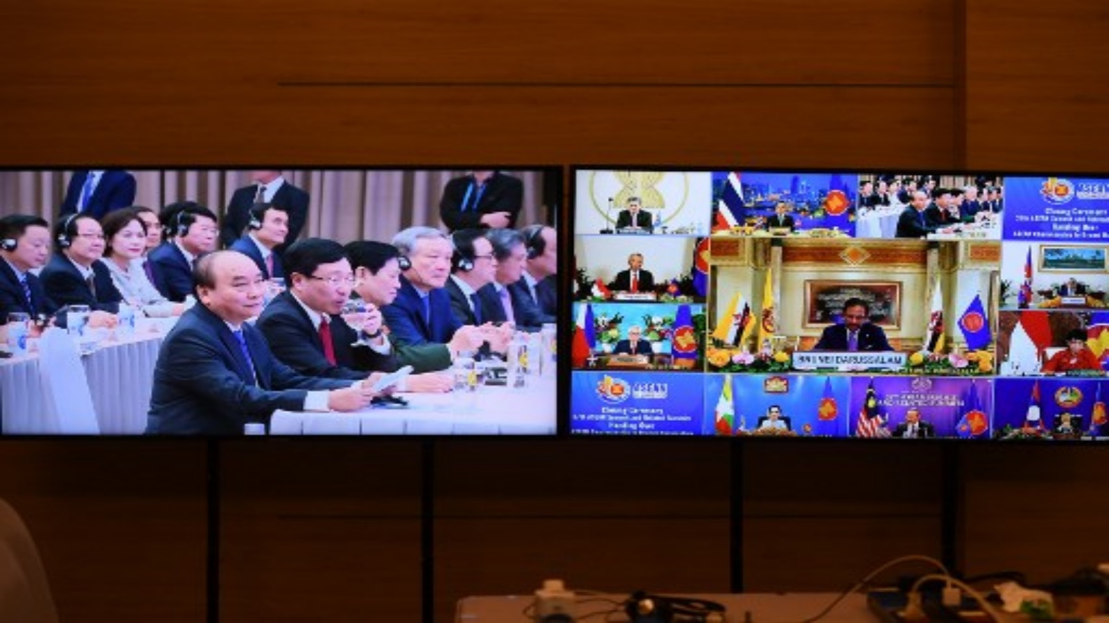 رئيس الوزراء الفيتنامي نجوين شوان فوك ينظر إلى قمة رابطة دول جنوب شرق آسيا (آسيان) التي تستضيف قمة بروناي سلطان حسن البلقية (الثاني إلى اليمين) ، كما يظهر على شاشات التلفزيون ، وهي تخاطب حفل اختتام رابطة دول جنوب شرق آسيا في هانوي في 15 نوفمبر 2020.