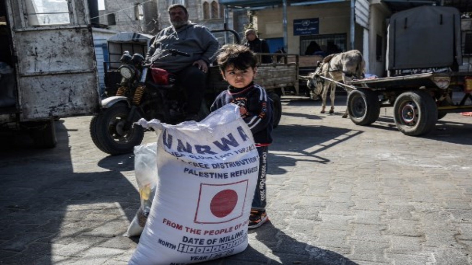طفل يقف بجانب كيس دقيق بينما يأتي الناس لتلقي مساعدات غذائية من مركز توزيع تابع لوكالة غوث وتشغيل اللاجئين الفلسطينيين (الأونروا) في مخيم خان يونس للاجئين الفلسطينيين في جنوب غزة مطلع العام الحالي