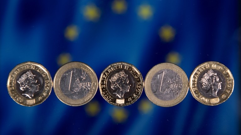 صورة من الأرشيف لعملة معدنية من الجنيه الاسترليني وأخرى من اليورو أمام علم للاتحاد الأوروبي