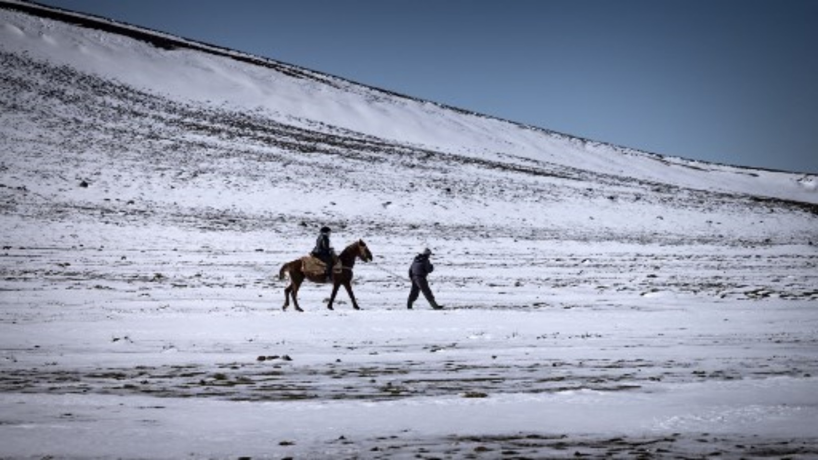 مرشد خيول محلي يمشي مع سائح يمتط على الجليد في مدينة أزرو ، على بعد حوالي 89 كيلومترًا جنوب فاس بإقليم إفران شمال المغرب في جبال الأطلس ، في 8 فبراير 2021.