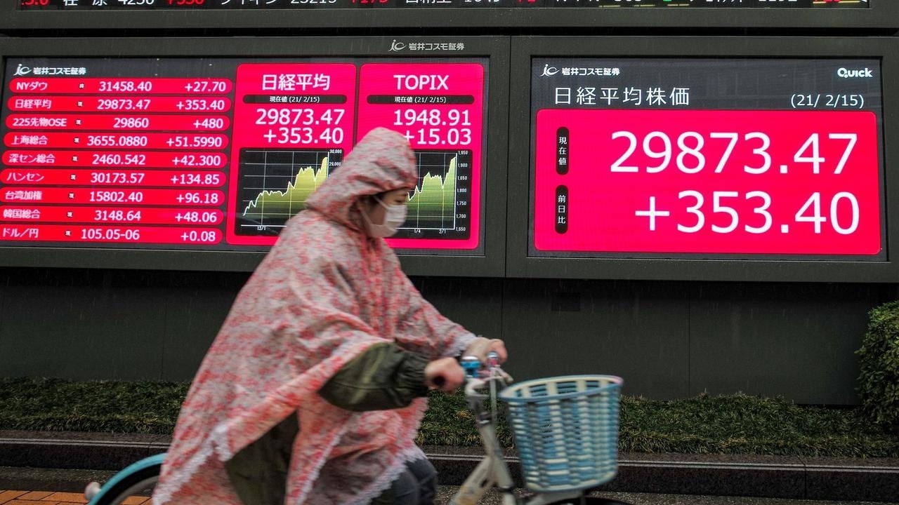 امرأة على دراجة هوائية تمر من أمام لوحة إلكترونية تظهر أسعار الأسهم في طوكيو بتاريخ 15 شباط/فبراير 2021