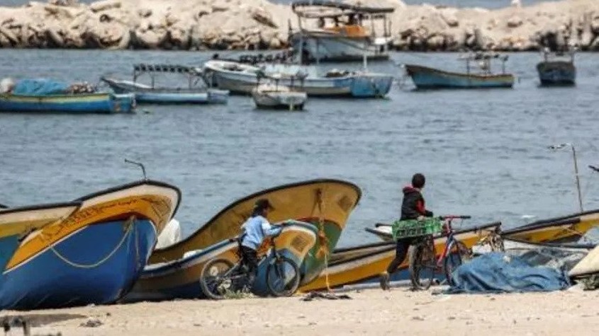  أولاد فلسطينيون يسيرون مع دراجاتهم الهوائية بالقرب من مراكب الصيادين في ميناء قطاع غزة في 26 نيسان/أبريل 2021، وأعلنت إسرائيل الإثنين اغلاق منطقة الصيد بالكامل قبالة قطاع غزة المحاصر