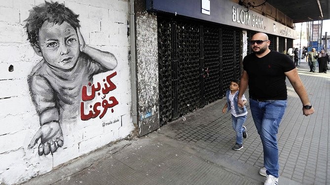 لبناني ونجله يمران أمام رسم غرافيتي في طرابلس موجه إلى السياسيين الذين يتهمه الشعب اللبناني بالفساد وهدر الأموال