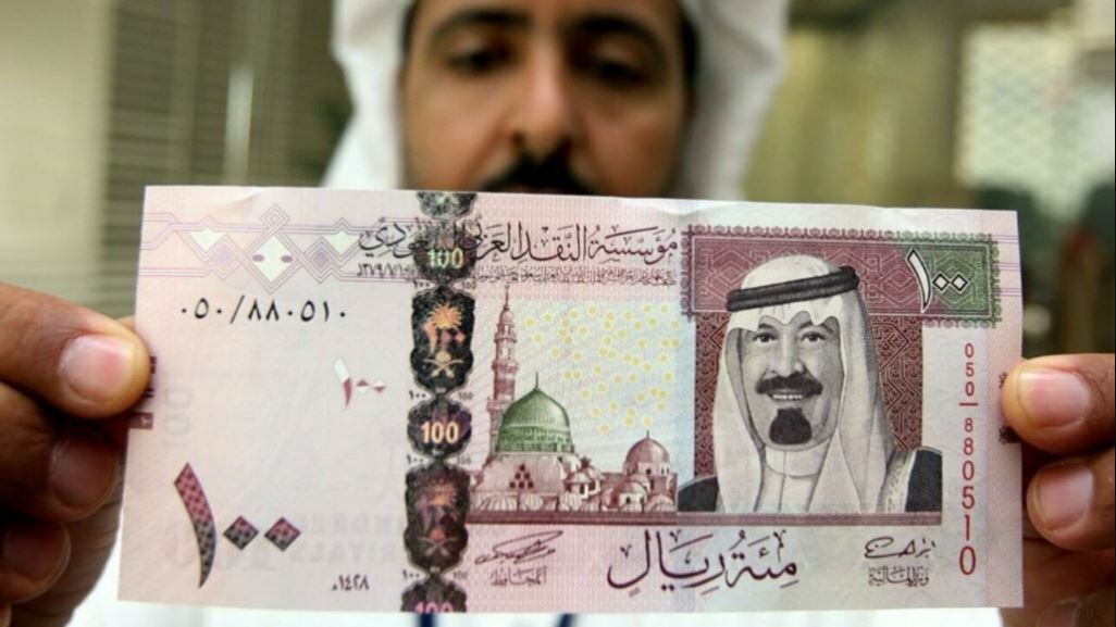 موظف سعودي يحمل ورقة نقدية من فئة 100 ريال