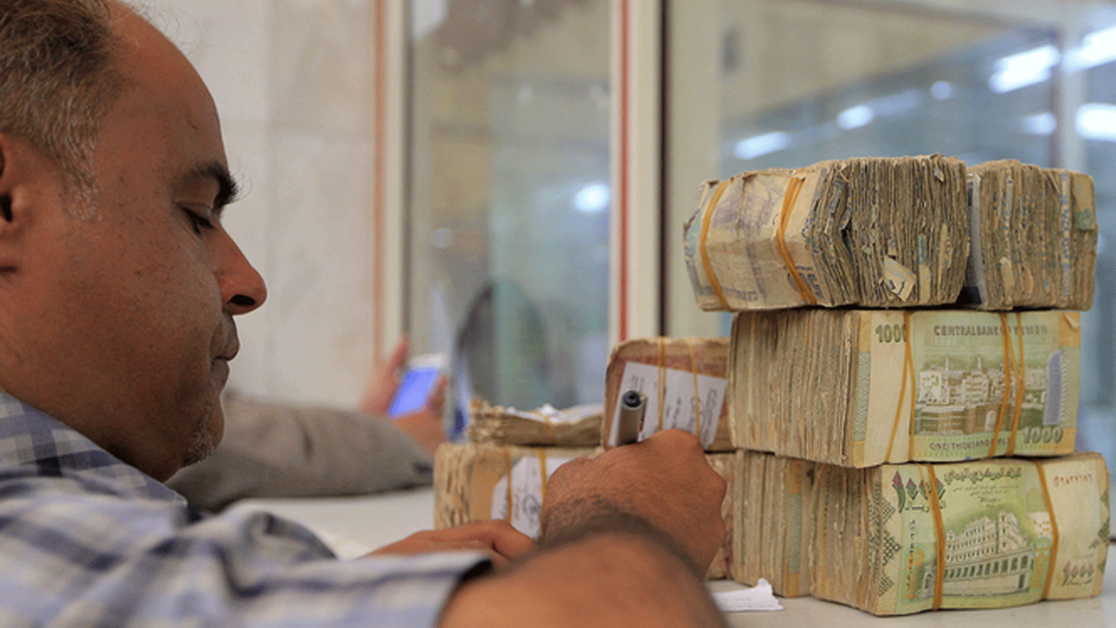موظف بالبنك المركزي اليمني يكتب ورقة بجانب أكوام من العملة اليمنية في مقر البنك بصنعاء في 23 حزيران/ يونيو 2021