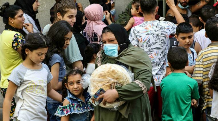 امرأة تغادر الفرن وهي تحمل ربطة خبز فيما ينتظر الناس دورهم أمام فرن في منطقة النبعة في بيروت