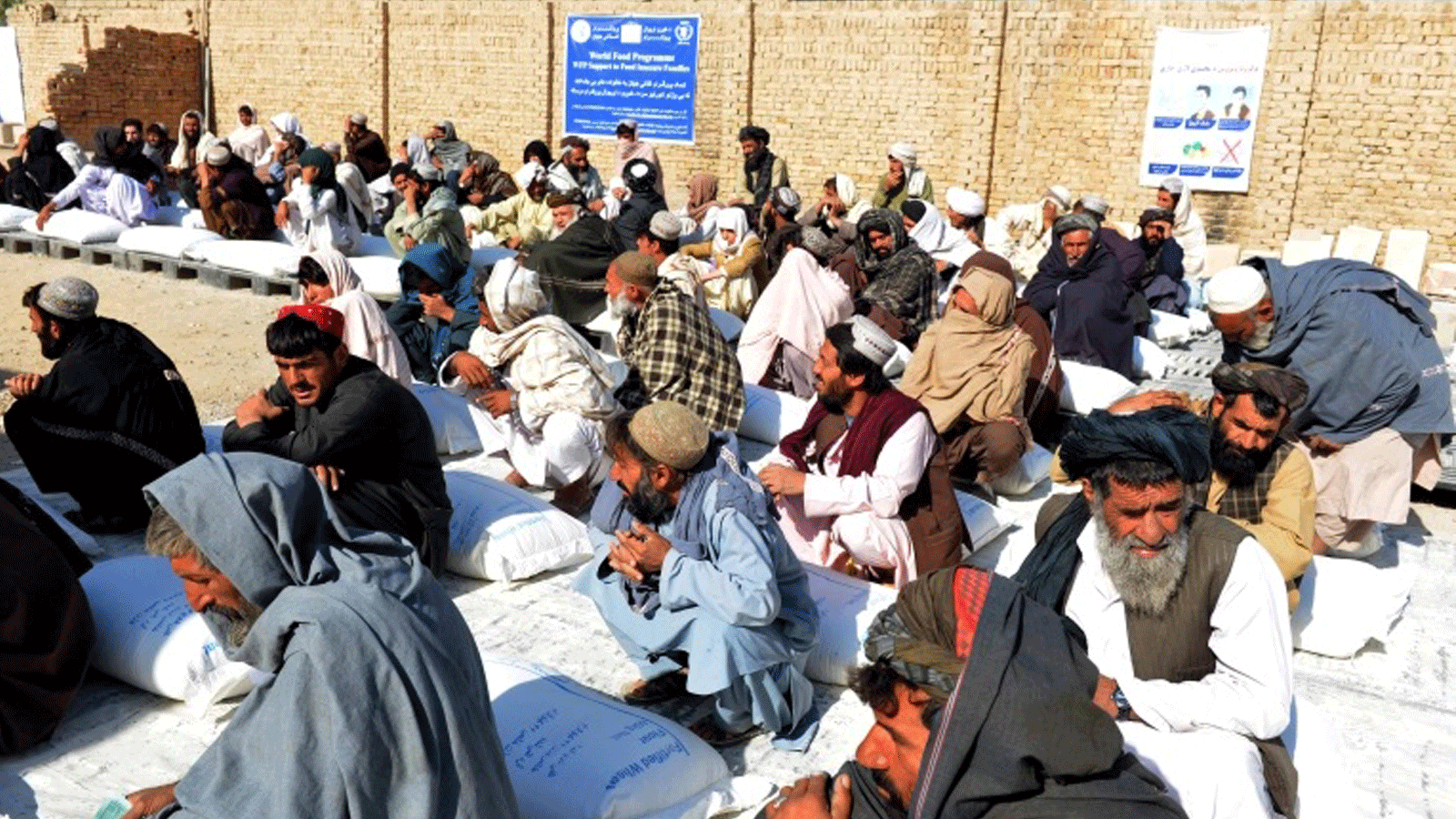 أفغانيون يجلسون بجانب أكياس الحبوب الغذائية التي تم توزيعها كمساعدات