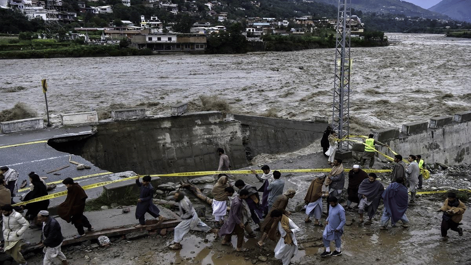 الناس يتجمعون أمام طريق تضررت بسبب مياه الفيضانات بعد هطول أمطار موسمية غزيرة في منطقة ماديان في وادي سوات شمال باكستان في 27 آب\أغسطس 2022