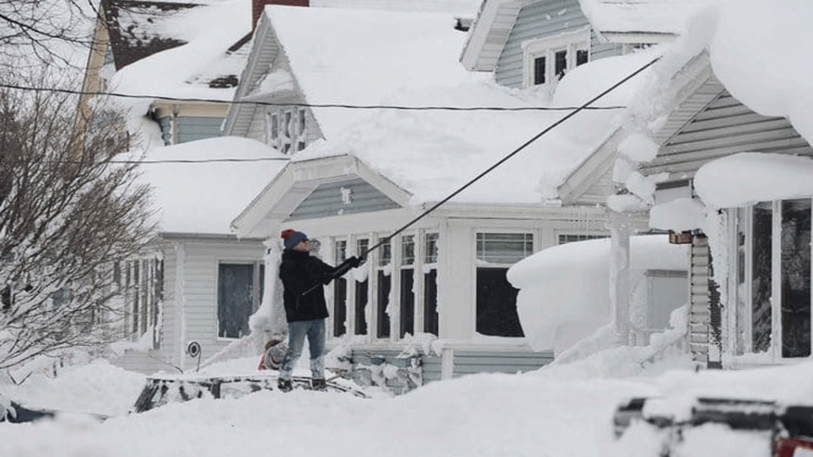 رجل يحاول إزالة الجليد من سقف منزله في 26 كانون الأول\ديسمبر 2022 في بوفالو ، نيويورك