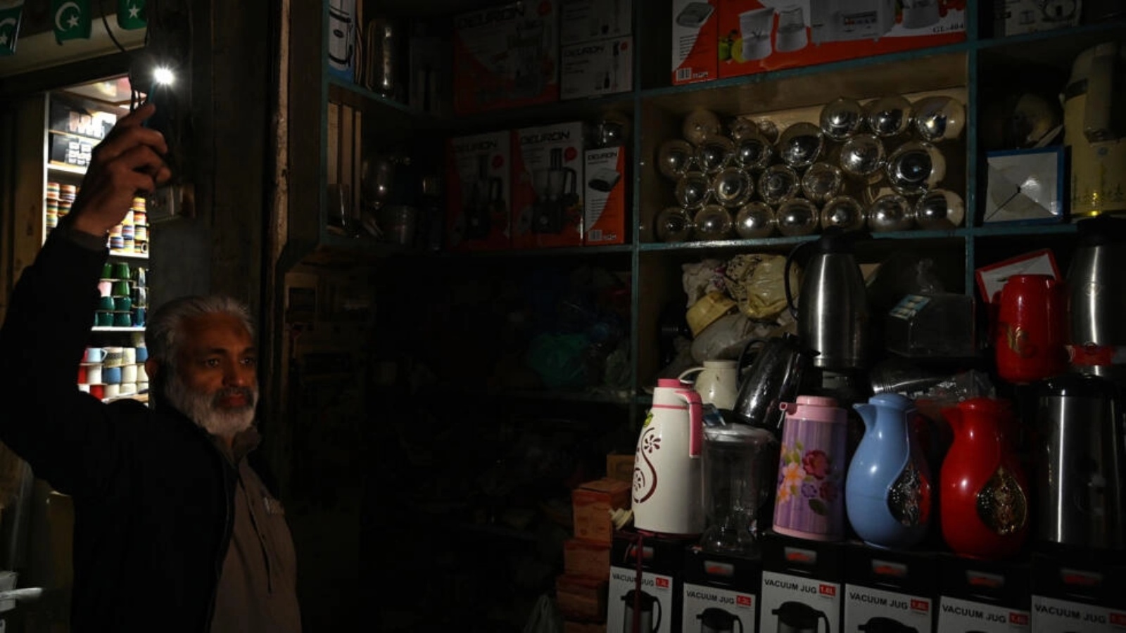 صاحب متجر في روالبيندي يستخدم ضوء هاتفه النقال في ظل انقطاع واسع النطاق للتيار الكهربائي في باكستان في 23 يناير 2023
