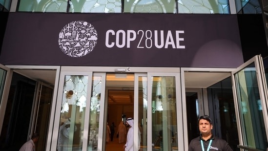 أشخاص يسيرون تحت لافتة COP28 في مكان انعقاد قمة الأمم المتحدة للمناخ في دبي