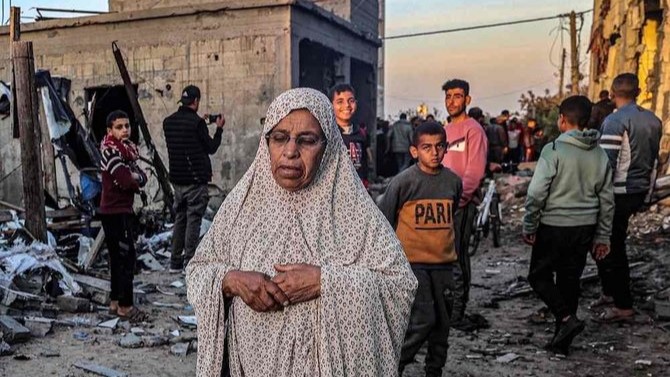 امرأة مسنة تسير أمام شبان بالقرب من المباني التي تضررت بشدة جراء القصف الإسرائيلي في رفح بجنوب قطاع غزة في 11 فبراير 2024