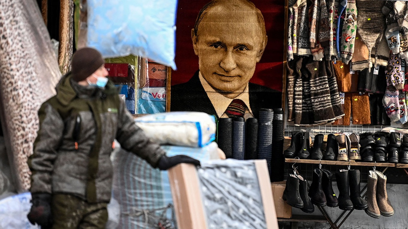 بائع يقف أمام صورة الرئيس الروسي فلاديمير بوتين في أحد أسواق موسكو