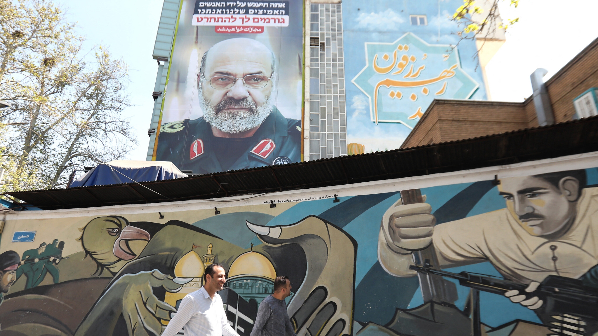 مارة في طهران أمام صورة للعميد محمد رضا زاهدي، الذي قتل في ضربة جوية في دمشق، مع شعار باللغة العبرية يقول 'سوف يُعاقب الفاعل'
