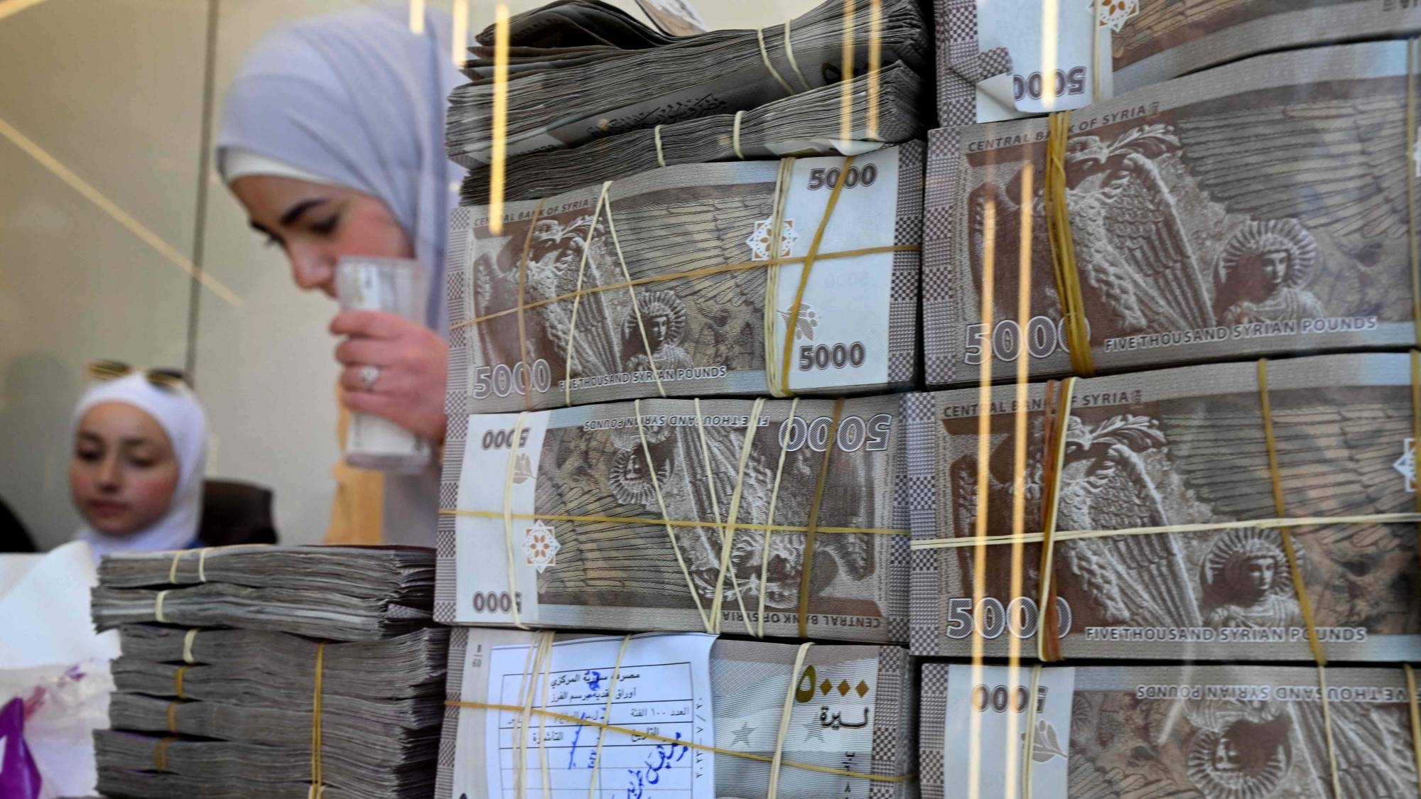 موظفون خلف أكوام من الأوراق النقدية المحلية أثناء خدمتهم للعملاء في محل صرافة بدمشق في 16 نيسان (أبريل) 2025