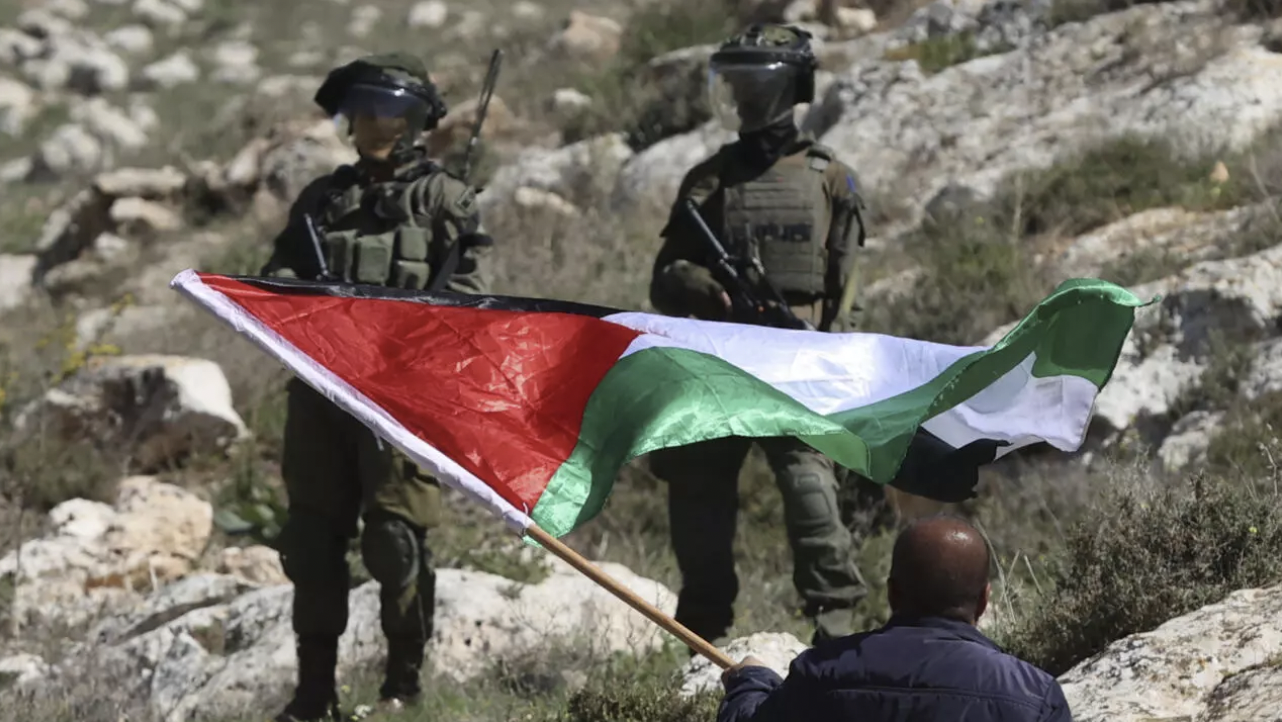 جنديان إسرائيليان في مواجهة متظاهر يلوح بالعلم الفلسطيني خلال احتجاج بالقرب من مدينة نابلس بالضفة الغربية المحتلة، في 10 آذار (مارس) 2023