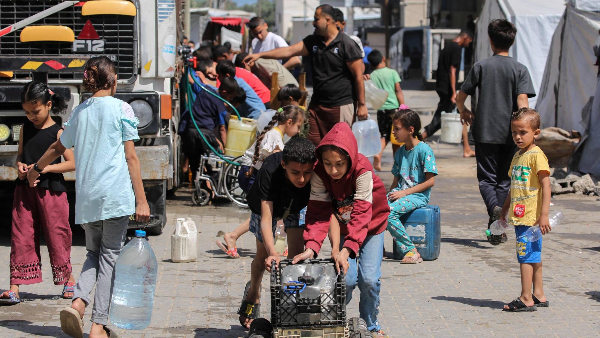 طفلان فلسطينيان ينقلان زجاجات مياه باستخدام عربة جر مرتجلة في مخيم النصيرات وسط قطاع غزة