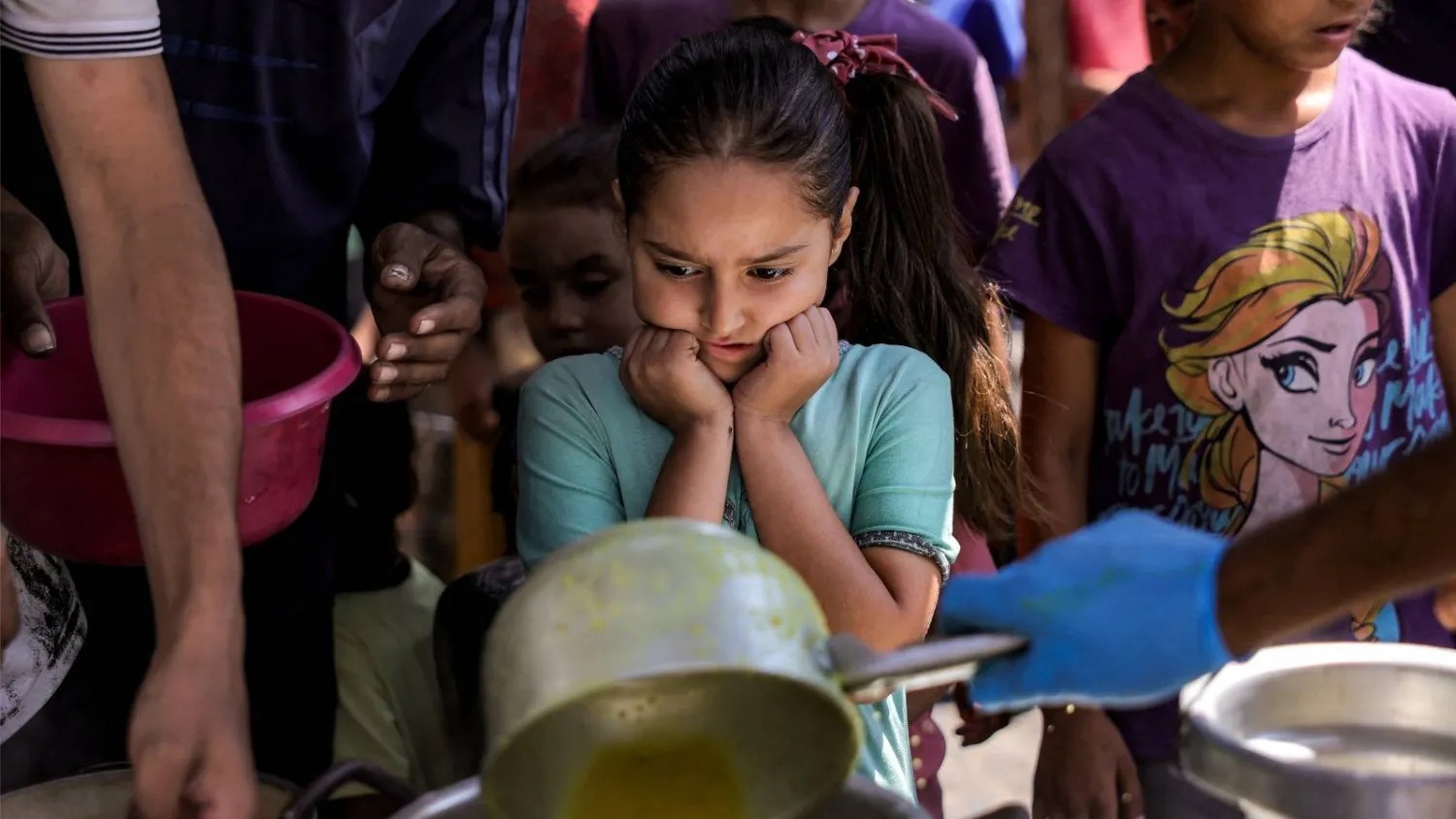 أطفال مع أوانٍ لتلقي وجبات الطعام من مطبخ خيري في مدينة غزة